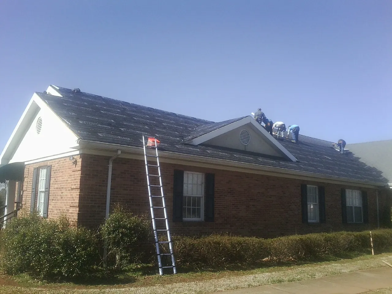 Crew tearing shingles off a brick ranch roof with a ladder set — Emergency Roof Repair work by our crew in New Bedford