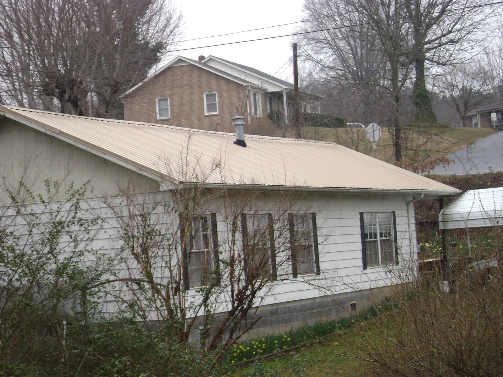 Tan metal roof on a white sided house set into a hillside — Commercial Roofing by Roofing Brothers in New Bedford